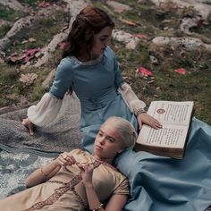 two women are laying on the ground with books in their hands and one is holding an open book