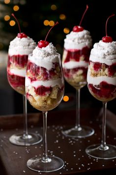 three desserts in wine glasses with cherries and whipped cream on the top are ready to be eaten