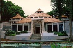 a building with thatched roof next to a body of water and trees in the background