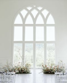 an empty room with chairs and flowers in front of a large window that overlooks the trees