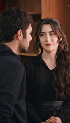 a man and woman standing next to each other in front of a book shelf with books on it