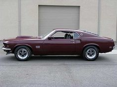 a maroon muscle car parked in front of a garage