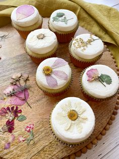 six cupcakes with white frosting and pink flowers on a wooden platter