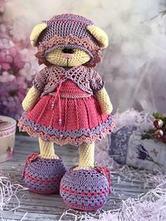 a crocheted teddy bear wearing a pink dress and booties on a table