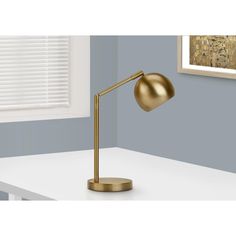 a gold desk lamp sitting on top of a white table in front of a window