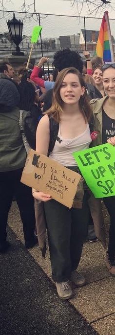 two girls holding signs in front of a group of people with flags and banners on the street