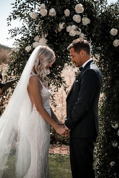 the bride and groom are getting married in front of an arch with flowers on it