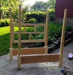 a wooden bed frame sitting on top of a stone patio next to a lush green yard