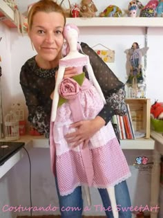 a woman holding a baby doll in her arms while wearing a pink and white dress