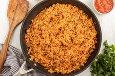 a skillet filled with rice next to some tomatoes and parsley on the side