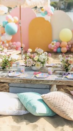 the table is set up on the beach with flowers and balloons in the background for an outdoor party