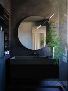 a black bathroom with a round mirror above the sink and a plant on the counter