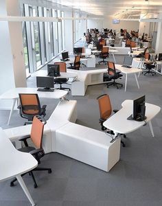 an office filled with desks and chairs next to each other in front of large windows