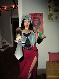 a woman dressed in costume holding a bottle and a pair of scissors while standing next to a couch