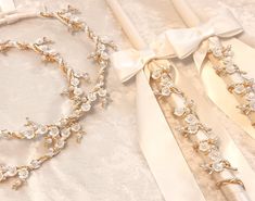 two pieces of jewelry are laying next to each other on a white cloth with bows