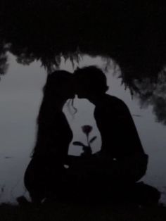 the silhouette of a man and woman kissing in front of a tree with flowers on it