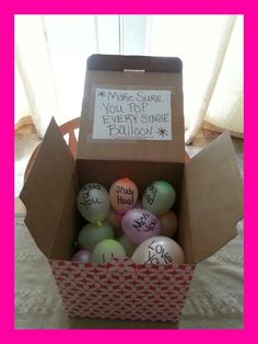 a cardboard box filled with lots of balls on top of a white bed covered in pink and green sheets