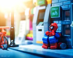 a lego spider man sitting on the ground next to a toy bike and vending machine