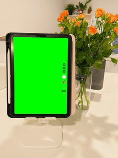 a green screen monitor sitting on top of a white table next to vases with orange flowers