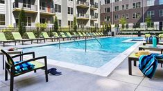 an outdoor swimming pool with lounge chairs around it and apartment buildings in the back ground