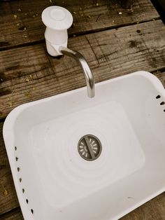 a white sink sitting on top of a wooden table next to a faucet