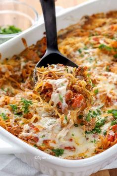 a casserole dish with meat, cheese and sauce being scooped from the casserole