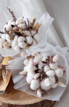 two bouquets of cotton flowers sitting on top of a piece of wood next to each other