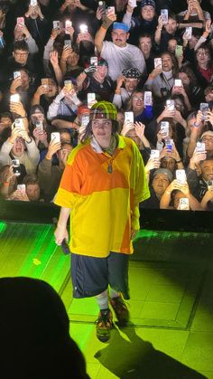 a man in an orange and yellow shirt is standing on stage with his cell phones