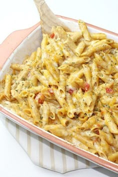 a casserole dish filled with pasta and sauce on a striped cloth next to a wooden spoon