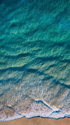 an aerial view of the ocean and beach with waves crashing on it's shore