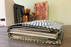 a stack of papers sitting on top of a wooden table next to a pen and pencil holder