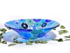 a blue glass bowl sitting on top of a white table next to green leaves and flowers