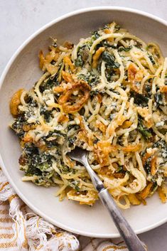 a white bowl filled with pasta and spinach on top of a table next to a fork