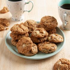 a plate full of cookies next to two cups of coffee