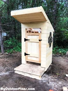 a wooden outhouse in the woods with an arrow pointing to it's door