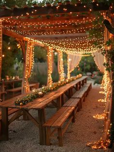 a wooden bench sitting under a canopy covered in lights and greenery with candles on it