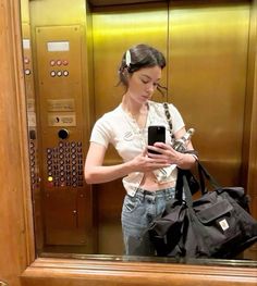 a woman standing in front of an elevator looking at her cell phone and holding a purse