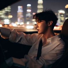 a man sitting in the drivers seat of a car at night with city lights behind him