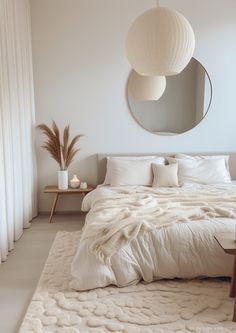 a bed with white sheets and pillows next to a round mirror on the wall above it