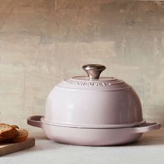 a white casserole dish sitting on top of a cutting board next to a loaf of bread