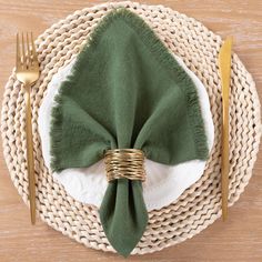 a place setting with green napkins, gold forks and silverware on a wicker plate