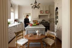 a woman standing in a kitchen next to a table with two chairs and a vase on it