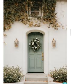 a green door with white flowers and greenery on the side of a house that has ivy growing over it