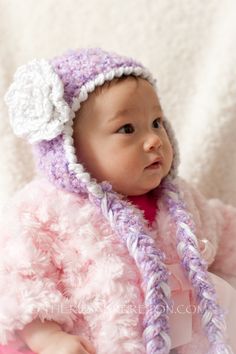 a baby wearing a purple and white hat with flowers on it's head sitting in a pink blanket