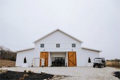 a truck parked in front of a white barn with two large doors on it's side