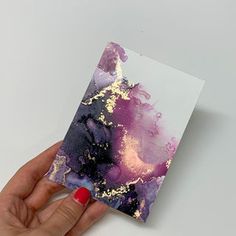 a hand holding up a card with purple and gold paint