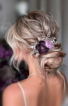 a woman with blonde hair wearing a purple flower in her hair and a braid updo