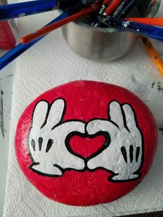 a painted rock with two hands making a heart on it and colored pencils next to it