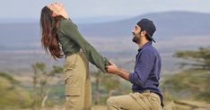 a man kneeling down next to a woman on top of a hill with trees in the background