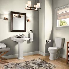 a white toilet sitting next to a sink in a bathroom under a mirror and light fixture